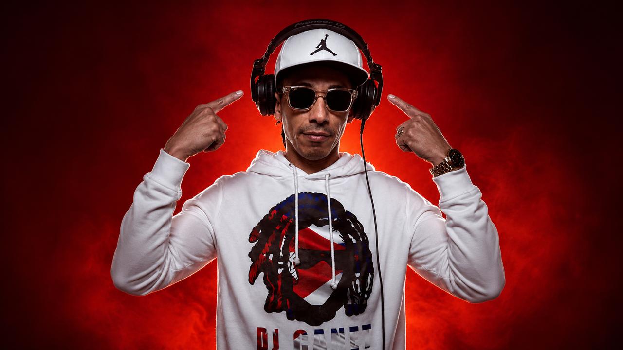 DJ Canet señalando con ambas manos los auriculares que lleva puestos, sobre humo rojo