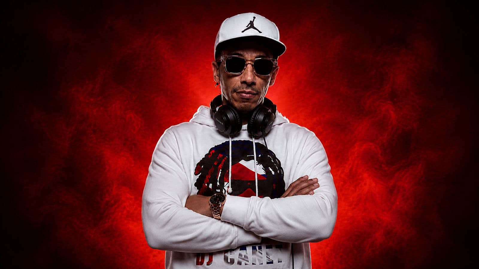 Amado Canet (DJ Canet) de frente con los brazos cruzados y los auriculares al cuello, sobre humo rojo