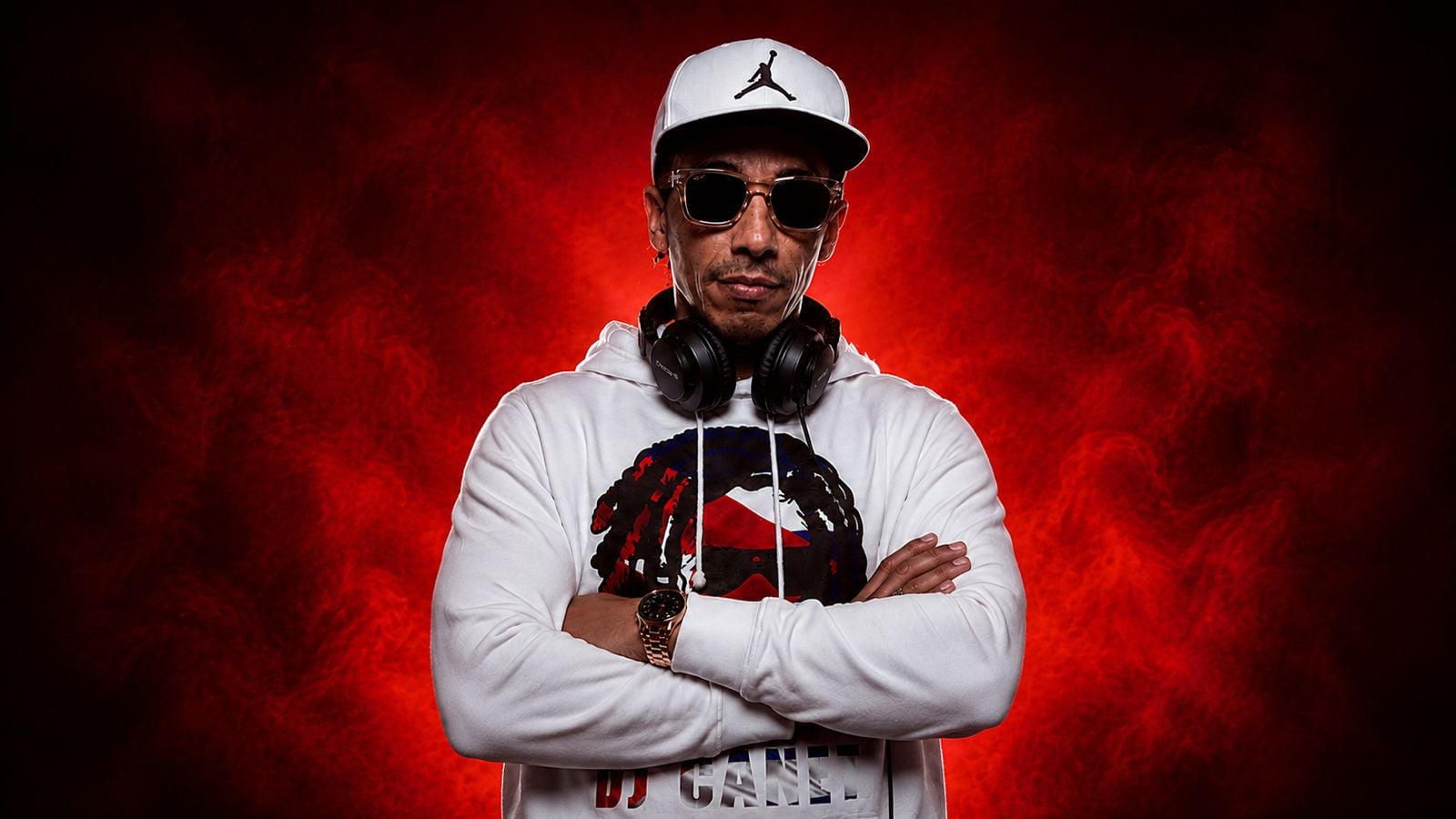 Amado Canet (DJ Canet) de frente con los brazos cruzados y los auriculares al cuello, sobre humo rojo